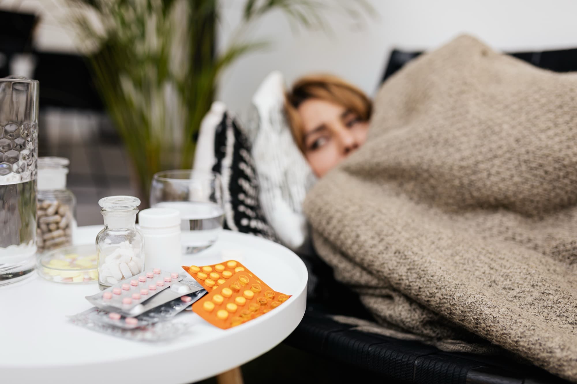 A person resting unwell at home with medications on a side table
